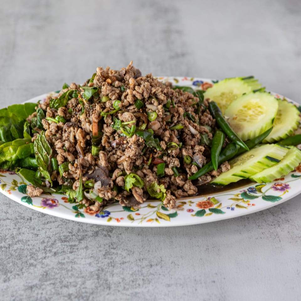 Lao minced meat salad (Larb) with fresh herbs, green chilies, and cucumber slices on a floral plate.