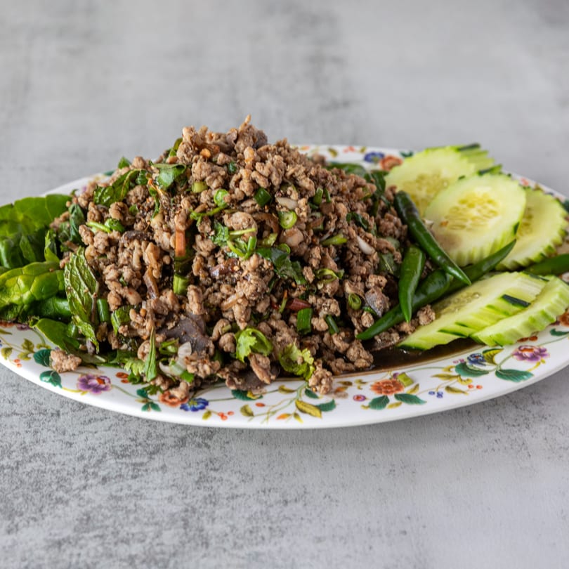 Lao minced meat salad (Larb) with fresh herbs, green chilies, and cucumber slices on a floral plate.