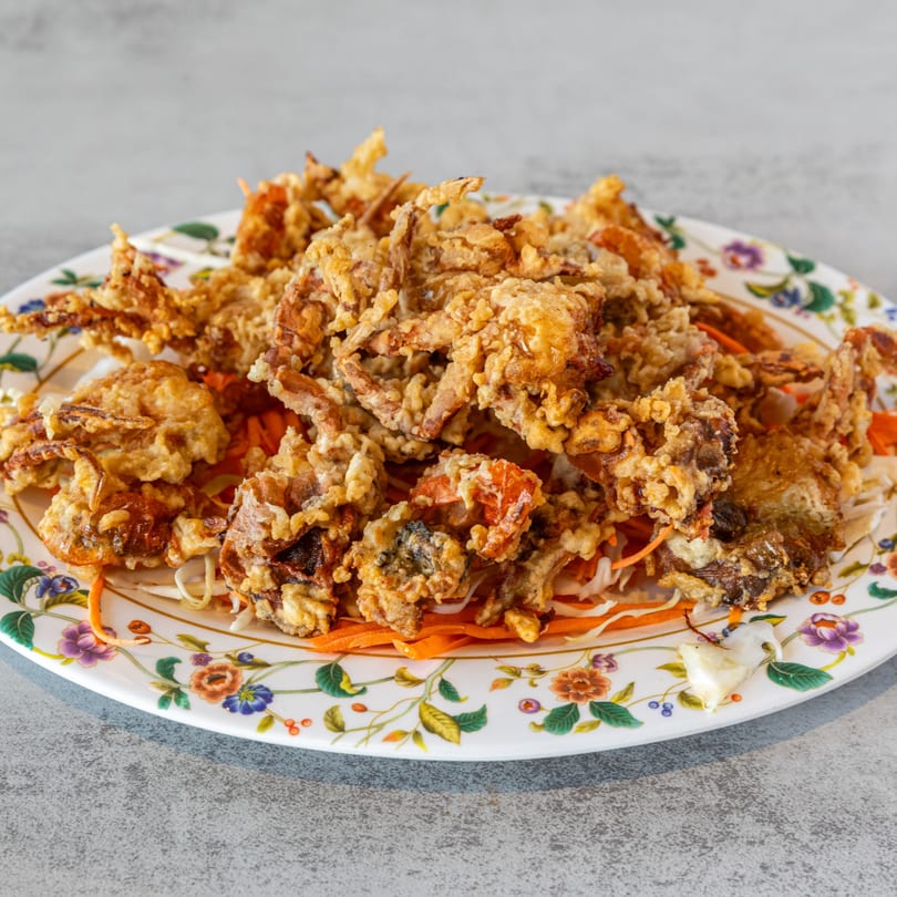 Crispy fried soft-shell crabs on a bed of shredded carrots and cabbage on a floral plate.