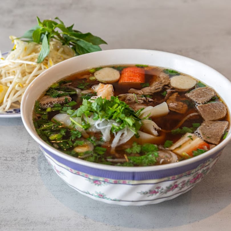 A bowl of Pho Lao Vieng's pho with various meats, noodles, and fresh herbs, with a side of bean sprouts.