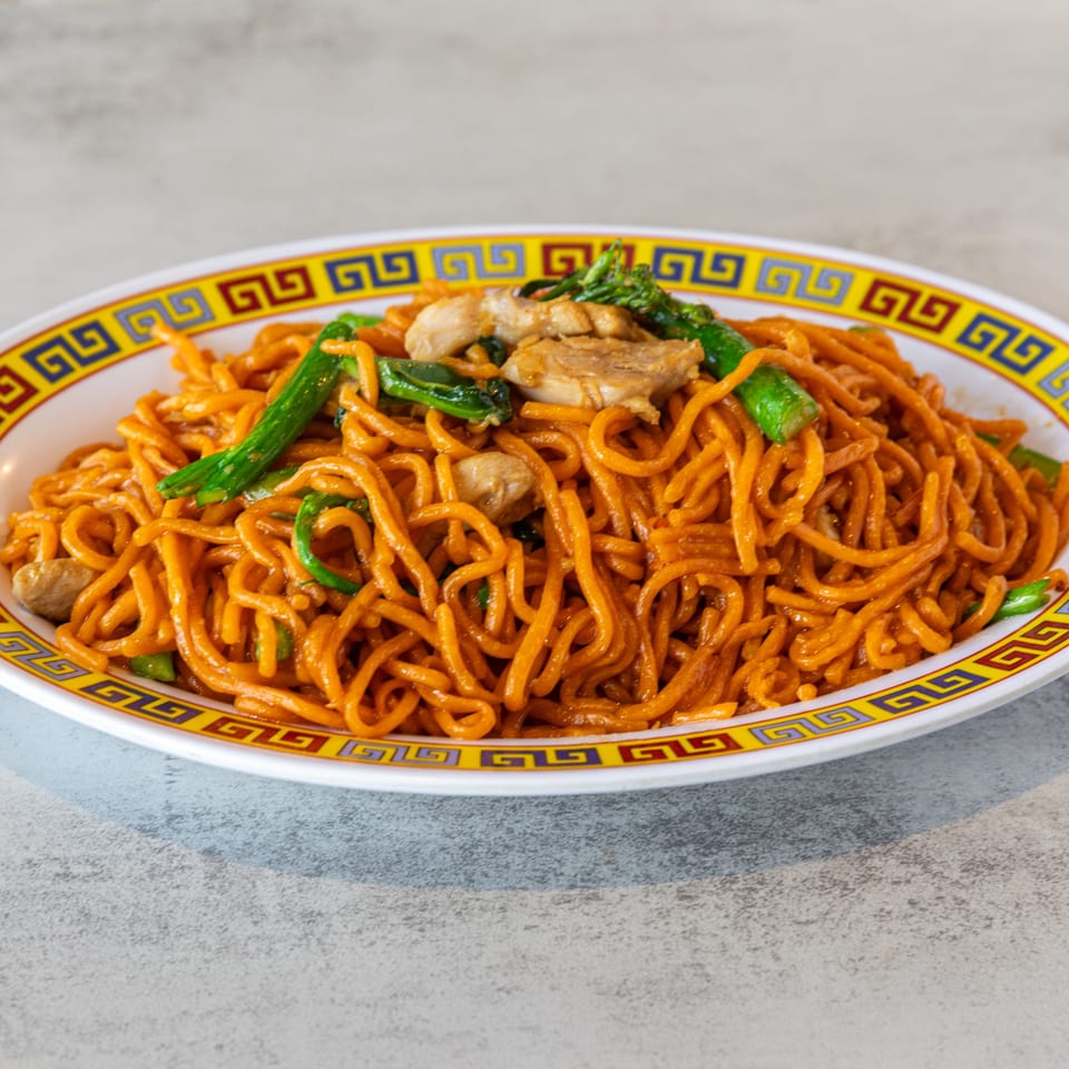 A plate of orange noodles with chicken and green vegetables, served on a decorative white and yellow plate.
