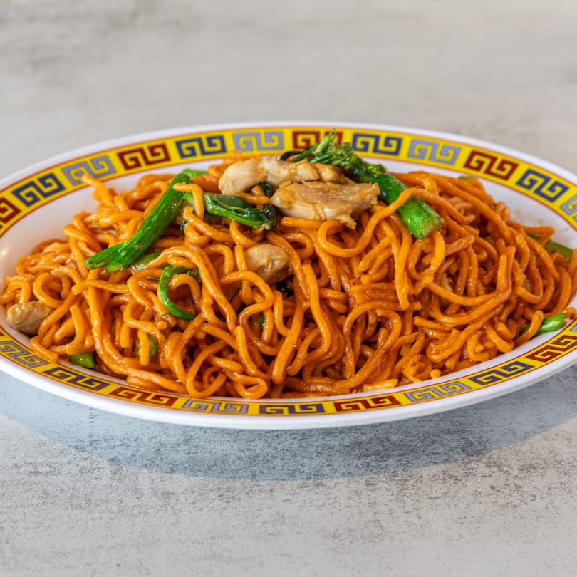 A plate of orange noodles with chicken and green vegetables, served on a decorative white and yellow plate.