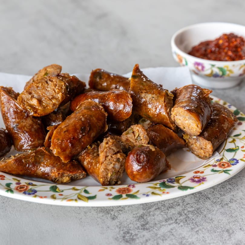 Platter of sliced Lao sausages, sai krok, with a small bowl of chili sauce in the background.