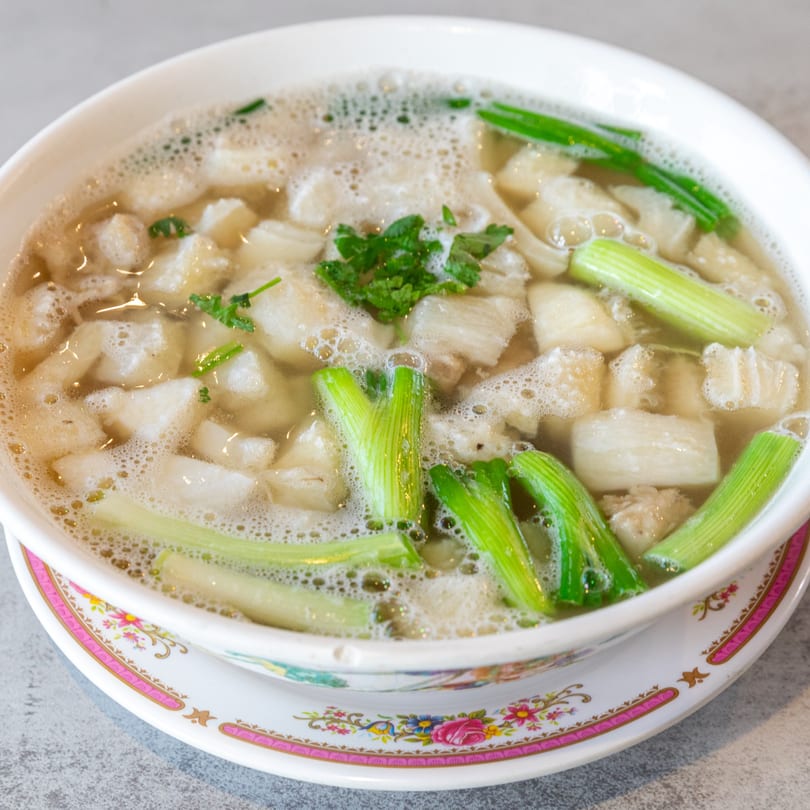 Close-up of a bowl of Pho Lao Vieng soup with meat, green onions, and cilantro.